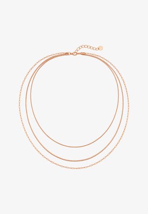 Delicado collar de cadena triple de oro rosa con cierre ajustable y pequeño charm en forma de flor sobre un fondo blanco.