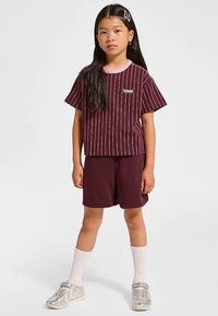 Vinröd randig kortärmad skjorta med rosa detaljer, tillsammans med matchande shorts. Vita knästrumpor och metallicfärgade sneakers fulländar outfiten.