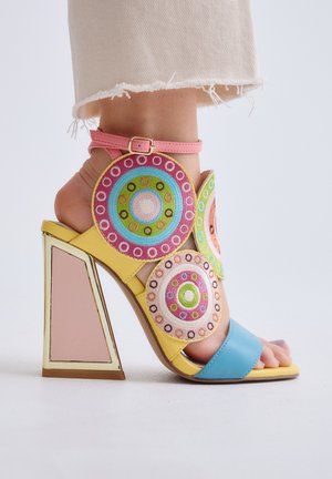Sandalia de tacón alto con tacón de bloque amarillo, tira azul en los dedos, tira rosa en el tobillo y decoraciones bordadas circulares y coloridas.