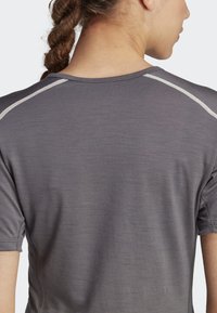 Gray short-sleeve top with a smooth texture. Features reflective accents on the shoulder seams and minimal stitching details.