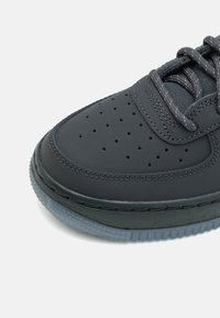 Zapatilla negra con parte superior de cuero suave y texturizado, caja de dedos perforada y acentos grises. Presenta una suela de goma translúcida.