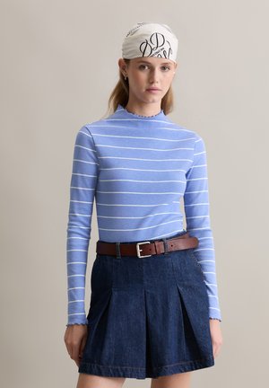 Blauw-wit gestreepte blouse met lange mouwen, gecombineerd met een donkerdenim rok met plooien, aangevuld met een bruine riem.