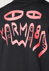 Black t-shirt featuring bold pink graphic design with eyes and the word "KARMA" in stylized lettering and hand illustrations.