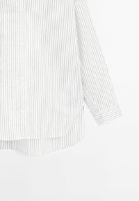 Camicia bianca con bottoni, a maniche lunghe e sottili righe verticali nere, con orlo curvo su sfondo bianco.