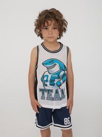 Bambino giovane con i capelli ricci che indossa una maglietta sportiva senza maniche bianca e nera e pantaloni corti blu con il numero 86.