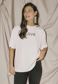 Bela majica s okroglim izrezom in kratkimi rokavi, ki vsebuje grafiko "LOVE" iz kristalov. V kombinaciji s temnimi jeans hlačami.