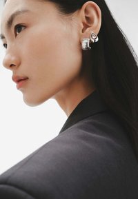 Pendientes de plata con forma de lágrima, adornados con una piedra preciosa transparente y un diseño grueso y estriado, exhibidos sobre un fondo neutro.