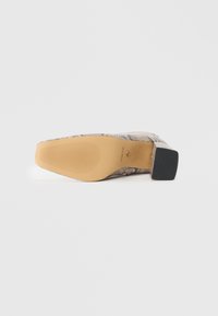 Vue de la semelle d'une chaussure carrée à motif de peau de serpent avec une semelle texturée couleur tan et un talon bloc noir, affichant le nom de la marque ALDO.