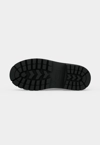 Semelle d'une botte noire robuste avec des crampons profonds et des motifs en zigzag conçus pour l'adhérence et la durabilité.
