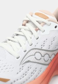 Baskets de course blanches avec un dessus en mesh, accents en argent et semelle orange. Comprend des lacets, un patch de logo et un motif texturé sur les côtés.