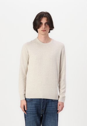 Ljusbeige pullovertröja med rund halsringning, långa ärmar, ribbad nederkant och mjuk textur, tillsammans med blå denimjeans.