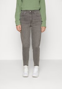 Vaqueros grises de talle alto con un corte ajustado, cinco bolsillos y un suave desvanecimiento, combinados con un suéter verde y zapatillas blancas.