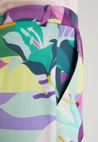 Kolorowa spódnica w kwiaty o żywym wzorze w odcieniach zieleni, fioletu, żółci i różu; wykonana z lekkiego materiału o gładkiej fakturze.