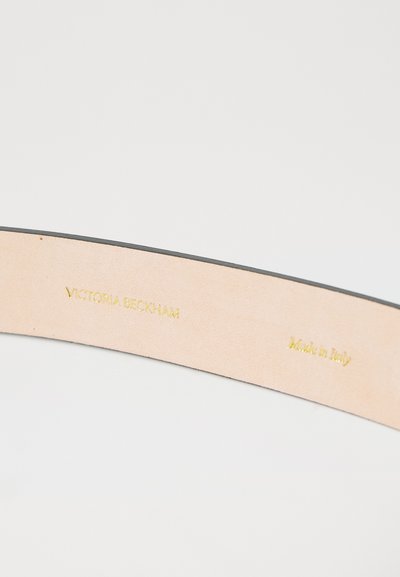 Heled nahk sisekujundus heledas beežis, millel on kullatud reljeefne tekst: "Victoria Beckham" ja "Valmistatud Itaalias." Must äär.