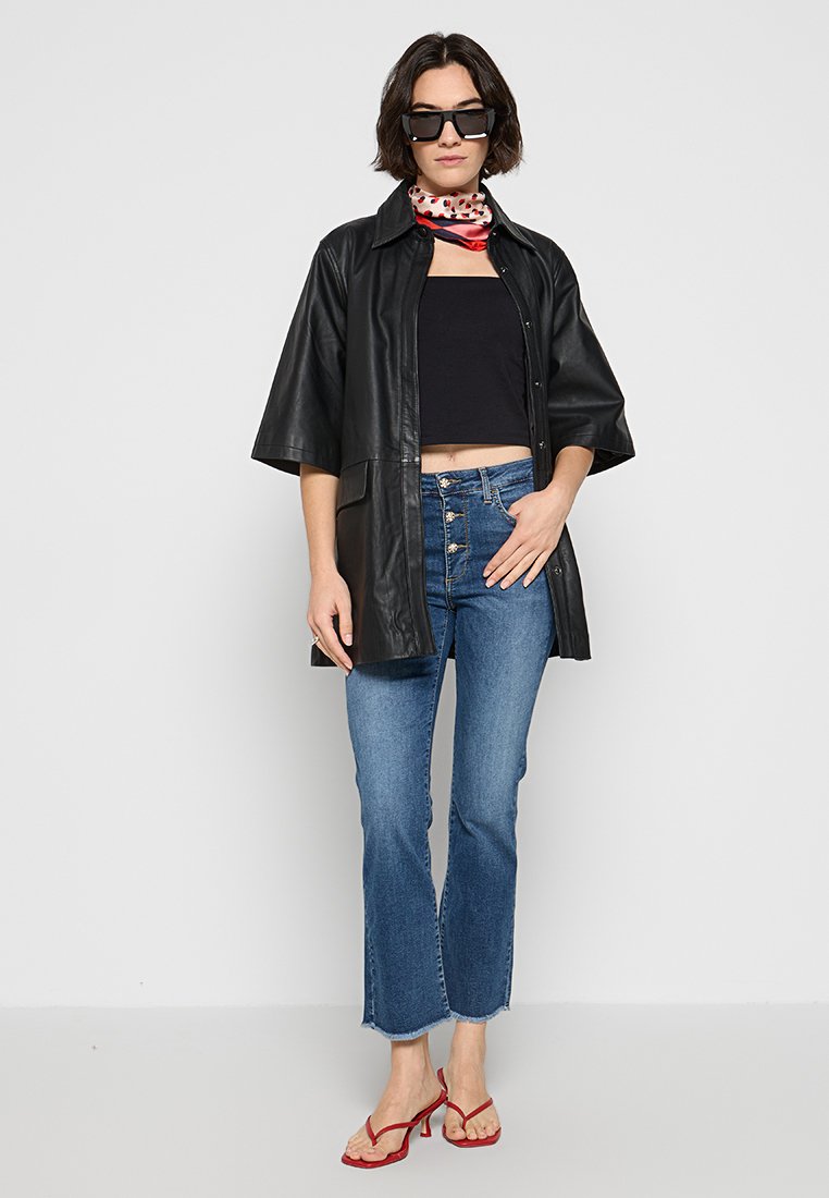 Schwarze Lederoversized-Hemden, eng anliegendes schwarzes Top, blaue hochgeschnittene Jeans, rote Sandalen mit Riemchen, gemusterter Schal um den Hals, Sonnenbrille.