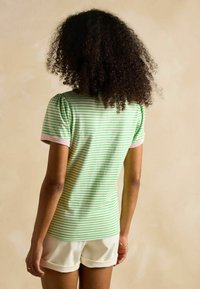 Green and white striped t-shirt with puffed sleeves and pink accents, paired with white shorts. Soft cotton material, casual cut.