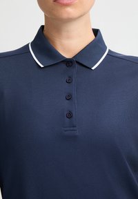 Polo shirt blu navy con colletto e una striscia accentuata bianca, sei bottoni neri e tessuto testurizzato.