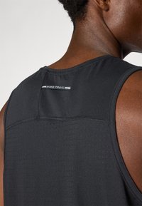 Black athletic tank top with a breathable textured fabric, featuring a rounded neckline and reflective "NIKE TRAIL" detail at the back.