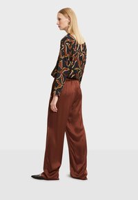 Pantalons larges en satin marron accompagnés d'un haut à manches longues noir avec un imprimé de feuilles colorées. La tenue comprend des chaussures plates noires.