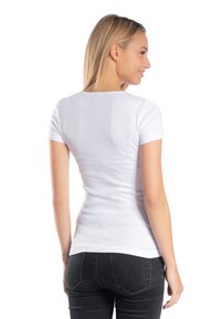 Biała dopasowana koszulka z krótkim rękawem, wykonana z miękkiej bawełny, z okrągłym dekoltem, noszona z ciemnymi dżinsami, prezentująca prosty, elegancki wygląd.