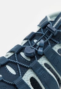 Blue athletic shoe with a textured mesh upper, flexible lacing system, and reinforced eyelets. Features rubber outsole with ventilation holes.