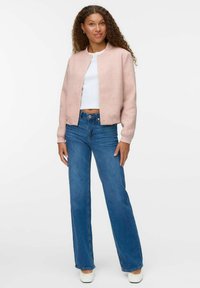 Chaqueta bomber de color rosa claro, hecha de tela suave, con botones a presión en el frente, combinada con pantalones de mezclilla flacos de cintura alta en azul y zapatillas blancas sin cordones.