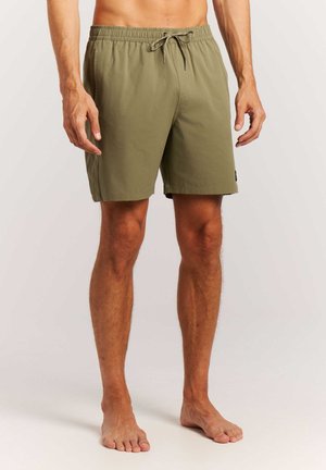 Męski model noszący oliwkowo-zielone szorty kąpielowe do kolan z elastycznym paskiem i sznurkiem, stojący boso na jednolitym tle.