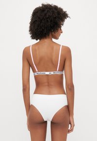 Balts bikini apakšda ar gludu tekstūru, kombinēta ar braleti, kurai ir rozā siksnas un melna zīmola elastīgā lente.