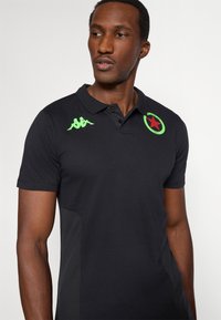 Fekete póló zöld díszítéssel, a mellrészen logóval és két gombbal a gallérnál; sima, könnyű anyagból készült.