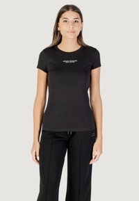 T-shirt nera realizzata in cotone liscio, con maniche corte e scollatura rotonda. Al centro, il testo bianco recita "ARMANI EXCHANGE."