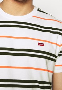 Witte t-shirt met korte mouwen, voorzien van groene en oranje horizontale strepen. Heeft een rode Levi's logo label op de linkerkant van de borst. Gemaakt van zacht katoen.