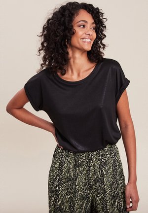Top noir à manches courtes en tissu lisse avec une coupe décontractée et un col rond, associé à un pantalon à motifs verts et noirs arborant des motifs de feuilles.