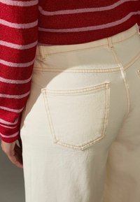 Jeans in denim chiaro con una tasca posteriore, abbinati a un maglione a righe rosse con righe rosa e bianche. Focus sulla texture e sulle cuciture.