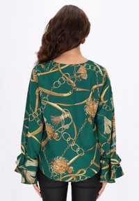 Zöld blúz aranylánc és díszminta mintázattal, hosszú ujjakkal, fodros részletekkel, sima anyagból, kerek nyakkivágással, laza szabással.