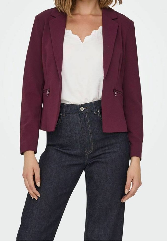 Blazer bordeaux au design ajusté, avec deux poches avant et une texture lisse, associé à un haut blanc à bords festonnés et un jean bleu marine.