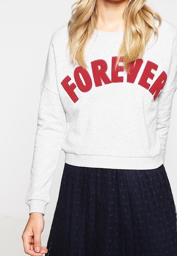 Sudadera gris con la palabra "FOREVER" en bordado rojo, escote redondo, mangas largas y puños de canalé, combinada con una falda oscura de textura.