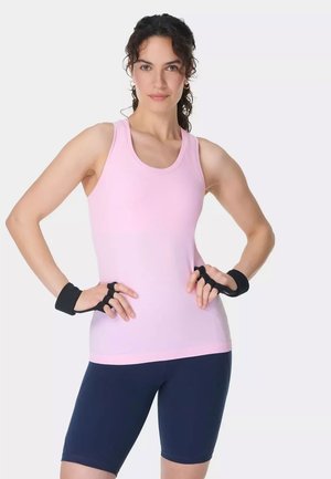 Woman standing confidently with hands on hips wearing pink sleeveless top, navy cycling shorts, and black fingerless workout gloves.