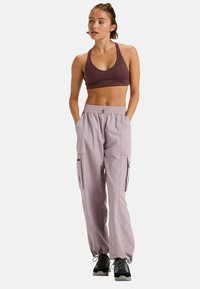 Pantalones cargo en lavanda clara con cintura elástica y bolsillos, combinados con un sujetador deportivo ajustado de color púrpura oscuro. Se llevan con zapatillas deportivas negras.