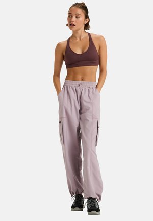Pantaloni cargo in un delicato lavanda con cintura elastica e tasche, abbinati a un reggiseno sportivo aderente di un viola scuro. Indossati con scarpe sportive nere.
