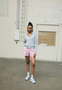 Light gray cable-knit zip-up sweater over a white top, paired with pink and white striped shorts and pastel blue sneakers.