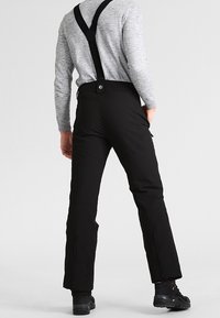 Mustat hiihtohousut säädettävillä mustilla olkaimilla, muotoiltu vyötärö, sivutaskut ja vetoketjulliset lahkeensuukohdat, jotka helpottavat niiden pukemista saappaiden päälle.