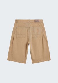 Shorts de couleur kaki arrivant aux genoux avec deux poches arrière dotées de motifs d’étoiles cousus et un écusson en cuir marqué « PXP » sur la taille.