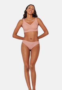 Sujetador inalámbrico seamless de color rosa claro y bikini a juego, fabricados con tejido suave, con una textura lisa y un diseño minimalista, sin hardware visible.