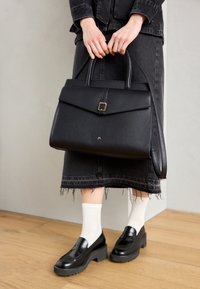 Schwarze strukturierte Handtasche mit einem Klappdeckel, goldener quadratischer Schnalle und doppelten Griffen. Aus glattem Leder; kombiniert mit einem schwarzen Denim-Rock und Loafers.