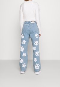 Jeans wide-leg in denim azzurro chiaro con ricami floreali bianchi lungo le gambe, vita alta e un'etichetta in tessuto nera "RAGGED" in vita.