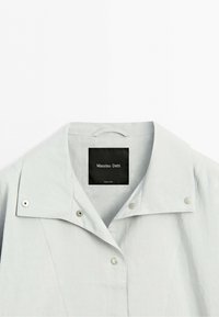 Biała kurtka z kołnierzem, zatrzaskami i czarną metką "Massimo Dutti" wewnątrz kołnierza.