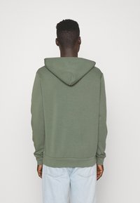 Zelená mikina s kapucí, dlouhými rukávy a žebrovanými manžetami a lemem. Jednoduchý design, vyrobená z měkké tkaniny, zobrazená zezadu.