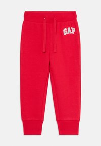 Pantaloni da bambino rossi in felpa con vita elasticizzata, cordino, polsini a coste e logo GAP bianco sulla coscia sinistra.