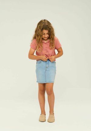 Kort rosa skjorta med uppvikta ärmar, matchad med en ljusblå denimkjol som har dekorativa vita prickar. Bruna slip-in skor.