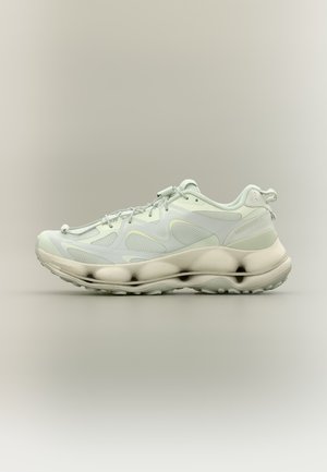Chaussure de sport gris clair et blanc avec panneaux en mesh, semelle épaisse et rembourrée, et languette au talon sur fond neutre.